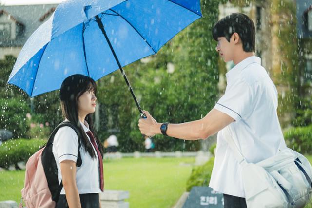 tvN 드라마 ‘선재 업고 튀어’에서 고등학생 남주인공 류선재(변우석·오른쪽)가 파란색 우산을 씌워주고, 여주인공 임솔(김혜윤)은 선재를 애틋하게 바라보고 있다. 두 사람은 비가 오는 날에 돌아가며 서로에게 우산을 씌워준다. tvN 제공