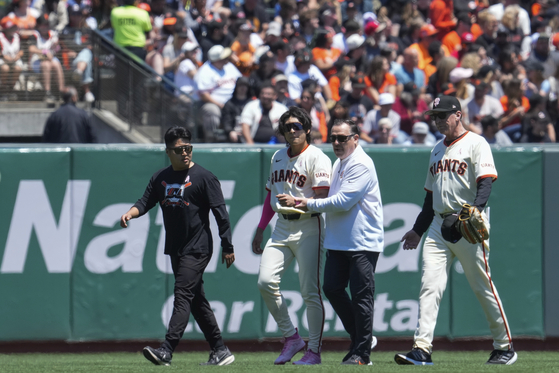 San Francisco Giants center fielder Lee Jung-hoo, second from left, is helped off the field following an injury during the first inning of a game against the Cincinnati Reds on Sunday at Oracle Park in San Francisco, California. [AP/YONHAP]