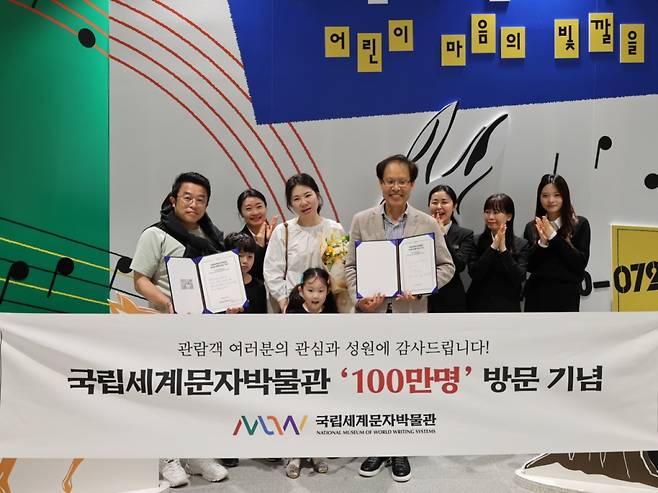 김성헌 박물관장이 100만명째 관람객 가족에게 기념품과 특별전시도록을 전달하고 기념사진을 찍고 있다/사진=국립세계문자박물관