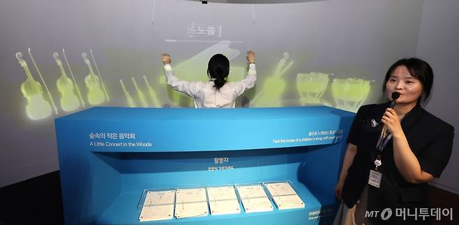 [인천=뉴시스] 전진환 기자 = 이정연 학예사가 29일 오후 '파란마음 하얀마음 - 어린이 마음의 빛깔을 노래하다' 기획특별전이 열리는 인천 연수구 국립세계문자박물관에서 지휘자가 되어 오케스트라라로 동요를 연주하는 미디어아트 체험을 소개하고 있다. 창작동요 100주년을 기념하여 열리는 이번 전시에서는 우리나라 첫 창장동요곡집 '반달' 초판본 등 34점의 자료와 24개국의 동요 105곡을 만날 수 있다.2024.04.29. amin2@newsis.com /사진=전진환