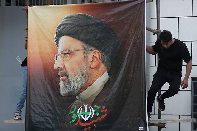 20일(현지시간) 이라크 바그다드 주재 이란 대사관 밖에서 한 남성이 전날 이란에서 헬기 추락사고로 세상을 떠난 고(故) 에브라힘 라이시 이란 대통령의 대형 초상화를 걸어 놓고 있다. [AFP]