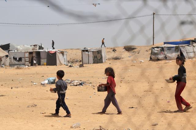 팔레스타인 어린이들이 19일 가자지구 남부 라파에서 식량 배급을 받은 냄비를 들고 걷고 있다. 라파=AFP 연합뉴스
