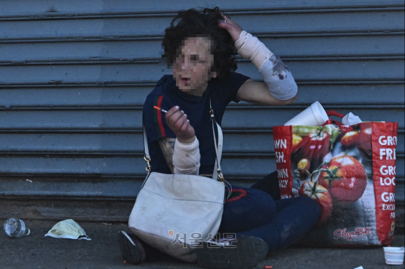 미국 펜실베이니아주 필라델피아 켄싱턴 거리에서 한 여성이 주사기를 든 채 주변을 응시하고 있다. 그의 양팔에는 마약 중독으로 썩은 피부를 보호하기 위한 붕대가 감겨 있다.