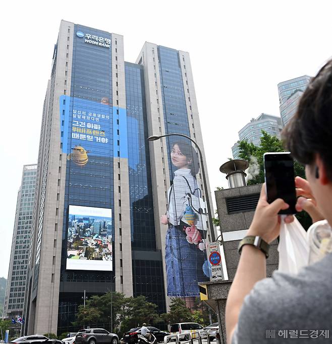 우리금융이 모델 아이유의 사진을 본점 건물 전체에 래핑한 24일 한 시민이 광고 사진을 촬영하고 있다. 이상섭 기자