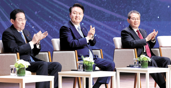 Korean President Yoon Suk Yeol, center, Japanese Prime Minister Fumio Kishida, left, and Chinese Premier Li Qiang, right, clap at the 8th South Korea-Japan-China Business Summit at the Korea Chamber of Commerce and Industry in central Seoul on Monday, after their trilateral summit. [JOINT PRESS CORPS]