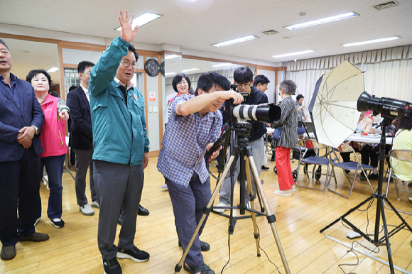 성산2동 주민센터 강당에서 어르신 장수사진 촬영이 진행돼 박강수 구청장(손든 이)이 어르신들의 사진 촬영을 돕고 있다. [사진=마포구]