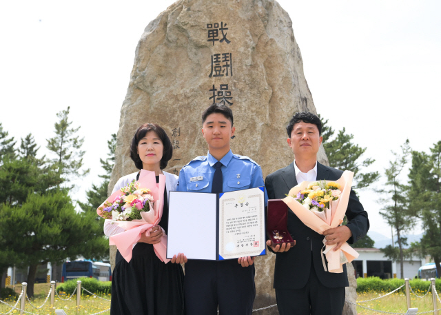 ▲ 고(故) 김여흥 병장의 유가족들이 18전비 상징물 앞에서 화랑무공훈장 증서와 메달을 들고 기념사진을 촬영하고 있다.(사진=공군 제18전투비행단 제공)