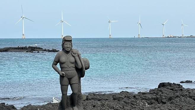 지난 3월 제주도 한경면 해안의 해녀 석상 뒤로 탐라해상풍력발전단지의 풍력발전기들이 돌아가고 있다. 연합뉴스