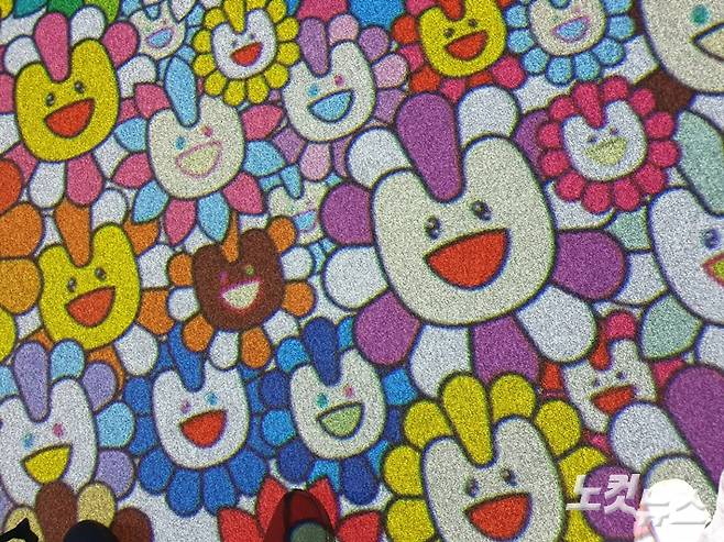 지하 1층에 마련된 미디어 공간에서는 뉴진스 곡 뮤직비디오 등 영상 콘텐츠가 끊임없이 나온다. 사진은 무라카미 다카시의 시그니처 '플라워' 캐릭터가 바닥까지 모든 공간을 채운 모습. 김수정 기자