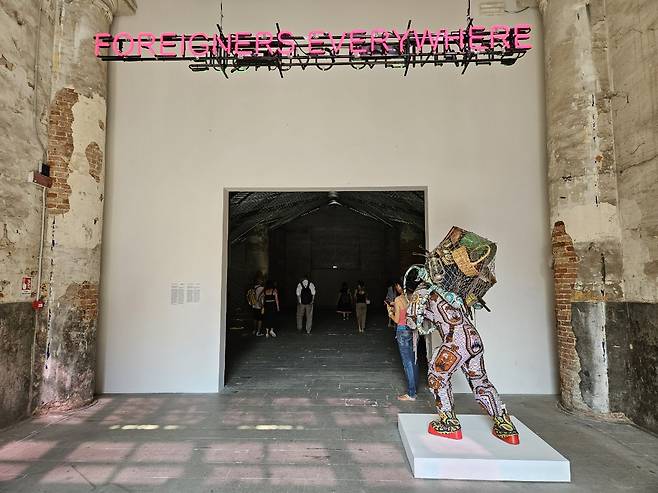 "Foreigners Everywhere (Self-portrait), Stranieri Ovunque (Autoritratto)" by Claire Fontaine (above) and "Refugee Astronaut VIII" by Yinka Shonibare (on the ground) are on display at the entrance to the biennale exhibition at the Arsenale in Venice on June 7. (Park Yuna/The Korea Herald)