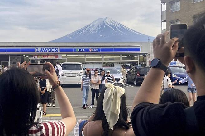 일본 야마나시현 후지카와구치코 마을에서 관광객들이 로손 편의점 뒤로 펼쳐진 후지산을 배경으로 기념촬영을 하고 있다. 뉴시스