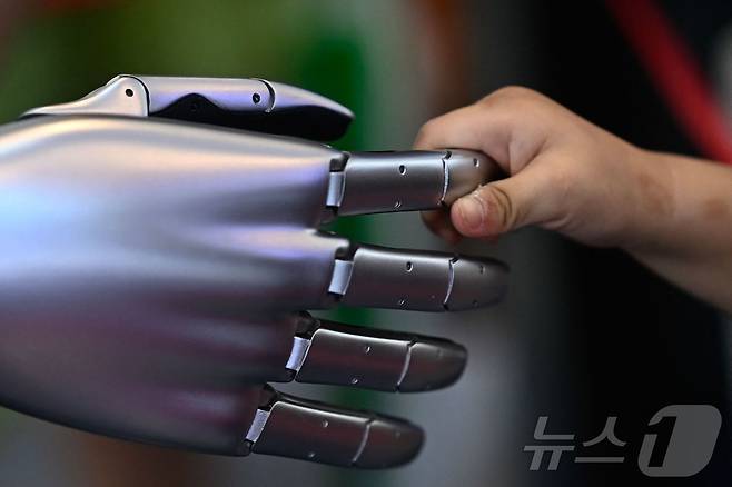 중국 톈진에서 23일(현지시간) 개최된 세계지능박람회에서 한 아이가 테슬라 휴머노이드 로봇의 손가락을 잡고 있다. 2024.06.23 ⓒ AFP=뉴스1 ⓒ News1 임여익 기자