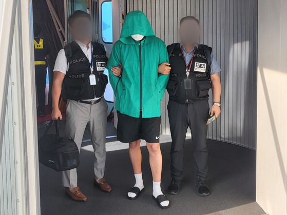 Two police officers escort a suspect who was extradited from Cambodia to Korea at Incheon International Airport on Wednesday morning. [THE NATIONAL POLICE AGENCY]