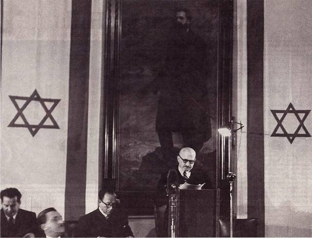 ▲ 테오도르 헤르츨에 이어 시오니즘 운동을 이끌었던 하임 바이츠만은 1948년 이스라엘 초대 대통령에 올랐다. 1949년 이스라엘 이민청에서 연설하는 바이츠만 뒤에 헤르츨의 대형 초상화가 걸려있다. ⓒ위키미디어