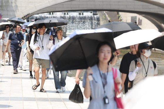 서울 지역 낮 최고 기온이 35도까지 올라 불볕더위가 찾아온 20일 서울 종로구 청계천에서 시민들이 양산을 펼쳐 따가운 햇빛을 막고 있다. [뉴스1]