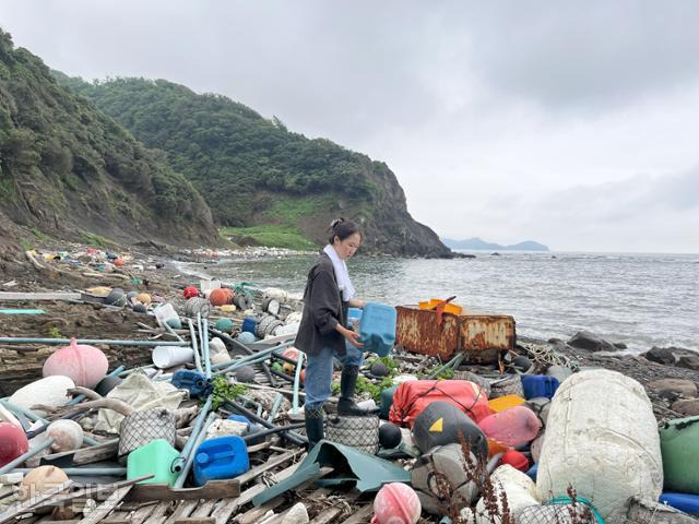 7월 11일 일본 쓰시마 구지카하마 해변에 쓰레기가 산을 이루고 있다. 본보 진달래 기자가 한국에서 온 것으로 보이는 파란 통을 들고 있다. 쓰시마=진달래 기자