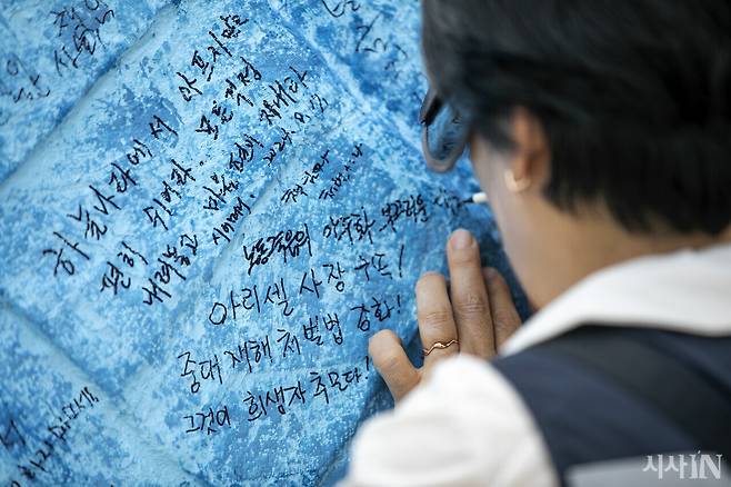 아리셀 참사를 상징하는 대형 하늘색 리본 모형에 한 참가자가 추모 메시지를 적고 있다. ⓒ시사IN 신선영