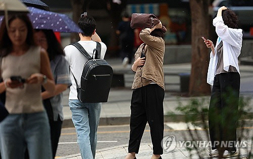 서울지역에 퇴근길 소나기가 내린 19일 오후 서울 세종로사거리 인근 버스정류장에서 우산을 준비하지 못한 시민들이 손과 가방으로 머리를 가린 채 버스를 기다리고 있다. [연합뉴스]