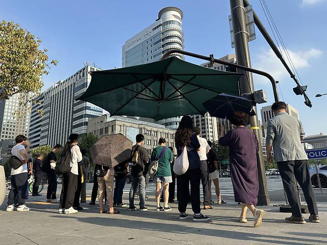 서울 전역에 폭염 경보가 발효된 10일 오후 서울 종로구 세종로 네거리 교차로에서 시민들이 그늘막 아래에서 더위를 피하며 신호를 기다리고 있다. 연합뉴스