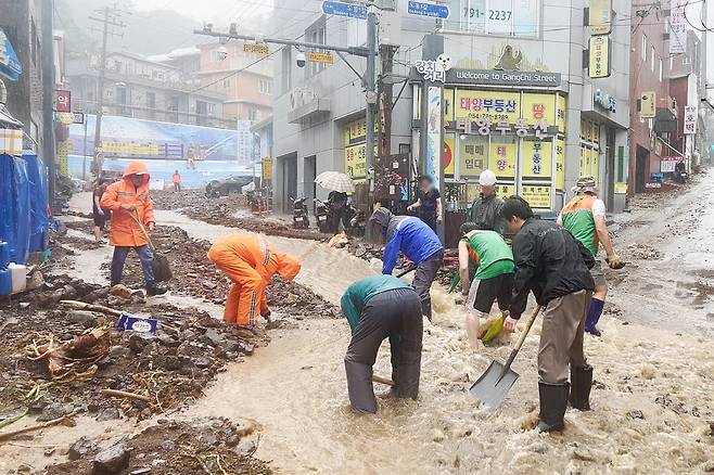 11일부터 12일까지 경북 울릉에 300㎜가 넘는 비가 내린 가운데 12일 오후 울릉 주요 도로에 빗물과 함께 토사가 흘러내리고 있다. 울릉군 공무원들은 주민과 함께 추가 피해를 막기 위해 토사를 치우고 있다. [연합]