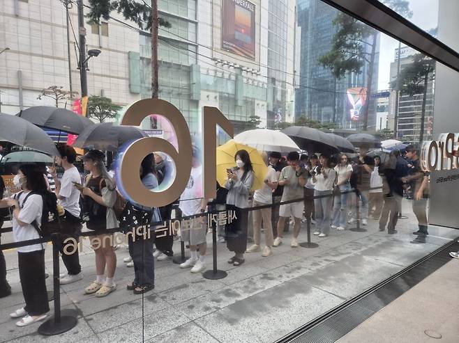 비가 오는데도 우산을 쓰고 아이폰16 시리즈를 수령하기 위해 기다리는 손님들. 사진=구자윤 기자