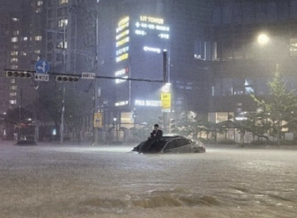 2022년 서울 강남 폭우로 침수된 차량 위에 체념한 모습으로 앉아 있어 화제가 된 남성. [사진=온라인 커뮤니티 ]