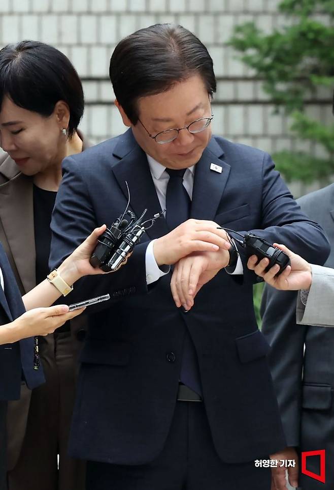 이재명 더불어민주당 대표의 공직선거법 위반 혐의에 대한 결심 공판이 20일 서울 중앙지방법원에서 열렸다. 이 대표가 법정에 들어가기 전 기자들의 질문을 들으며 시계를 보고 있다. 뒤에는 민주당 최고귀원과 당직자들이 서 있다. 사진=허영한 기자 younghan@