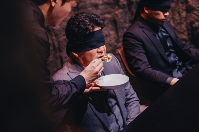 Star restaurateur Paik Jong-won, blindfolded, tastes a dish created by a contestant in "Culinary Class Wars." (Netflix)