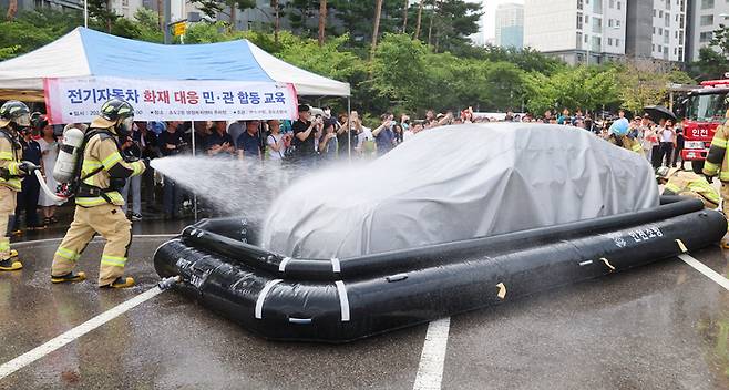 지난 8월 13일 인천 연수구 송도 2동 행정복지센터 주차장에서 열린 전기자동차 화재대응 민·관 합동 교육에서 소방관들이 질식소화덮개와 전기차 수조탱크를 이용한 전기차 화재 진압 모의 시연을 하고 있다. 연합뉴스