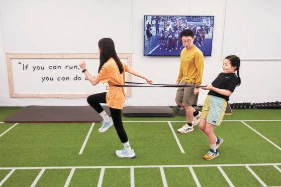 이안 학생기자가 앞으로 달려가려는 지우 학생기자의 허리를 감싼 고무밴드를 잡고 버티고 있다. 이 훈련은 코어 힘을 향상시키는 데 좋다.