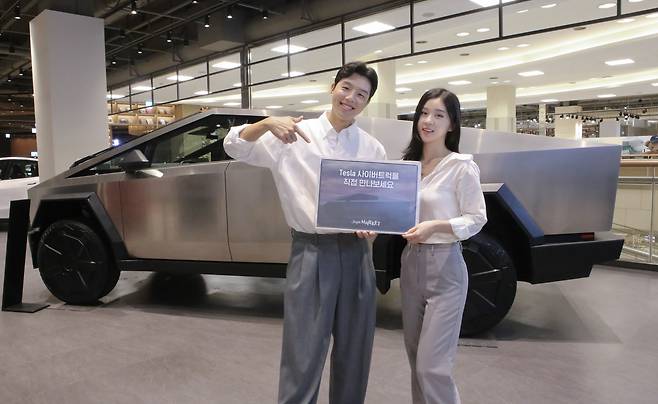 Models pose for photos in front of a Tesla Cybertruck parked at a pop-up event for the EV company in Starfield's Jukjeon branch in Yongin, Gyeonggi on Monday. [EMART]