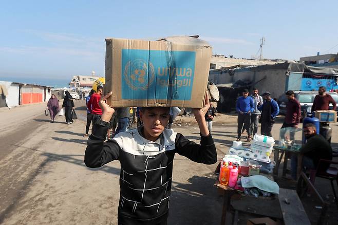 4일(현지시각) 가자지구 중부 다이르 알 발라흐에서 팔레스타인 소년이 유엔 구호사업국(UNRWA)이 배포한 구호 상자를 들고 가고 있다. 다이르알발라흐/로이터 연합뉴스