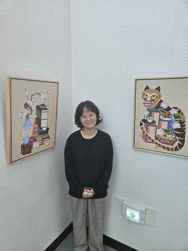 제주 서귀포 중앙도서관 전시장에서 36명의 작가가 참여한 ‘일상에 민화’ 전시회가 열렸다. 행사를 주최한 ‘제주그림’ 오은희 대표가 두 점의 ‘책거리도’ 사이에서 작품의 의미를 설명하고 있다.