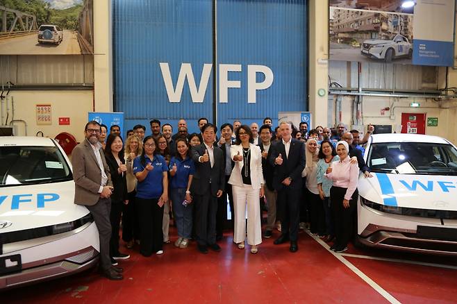 Sara Adam (center), UN World Food Programme director of management services; Lee Hang-soo (center left), Hyundai’s senior vice president of policy support; and Stephen Anderson (center right), director of WFP’s UAE office, pose with WFP staff alongside the donated Ioniq 5 vehicles at a handover ceremony in Dubai on Thursday. (Hyundai Motor Group)