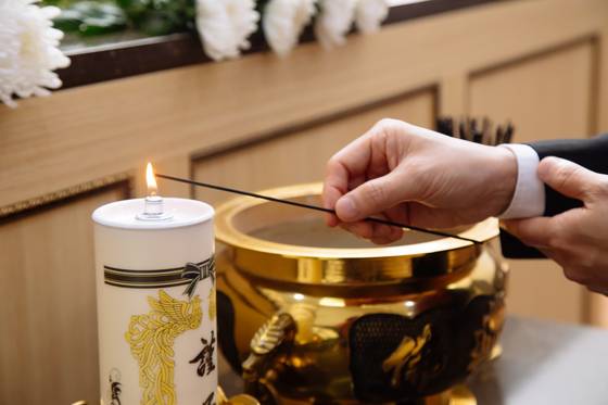 A person offers incense during a memorial service at a funeral. [GETTY IMAGES BANK]