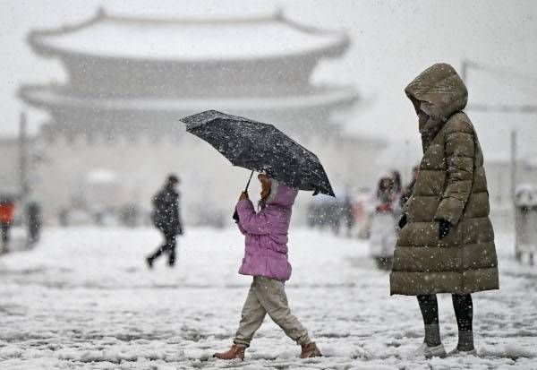 패딩으로 몸을 싸맨 가족이 27일 눈으로 뒤덮인 서울 종로구 광화문광장을 걷고 있다. 올여름 폭염과 북극 찬 공기를 머금은 절리저기압 등의 영향으로 이날 수도권에 폭설이 내린 것으로 분석된다. 윤웅 기자