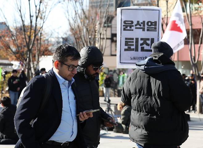 윤석열 대통령이 긴급 대국민 담화를 통해 비상계엄 해제를 선언한 4일 오전 서울 종로구 광화문광장에서 외국인 관광객들이 계엄 반대 집회를 지나치고 있다. 연합뉴스