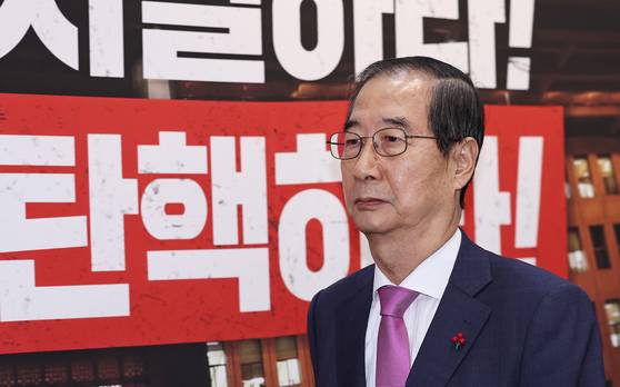 Prime Minister Han Duck-soo passes a banner calling for President Yoon Suk Yeol's impeachment as he leaves the main chamber of the National Assembly in Yeouido, western Seoul, on Tuesday. Han briefly attended Tuesday's plenary session to deliver the government's remarks on the 2025 budget after it had been railroaded through the legislature by the Democratic Party. [NEWS1]