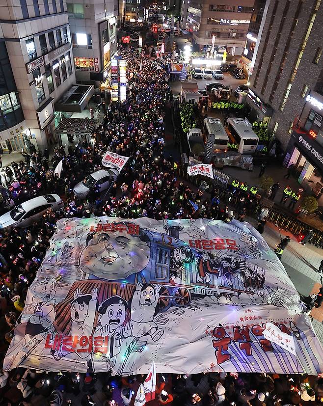 ‘윤석열 즉각 퇴진·사회대개혁 비상행동’ 주최로 13일 오후 서울 영등포구 국회의사당 인근에서 열린 탄핵소추안 국회 통과 촉구 촛불집회 참가자들이 국민의힘 당사 앞까지 행진해 현수막을 들고 있다. [연합뉴스]