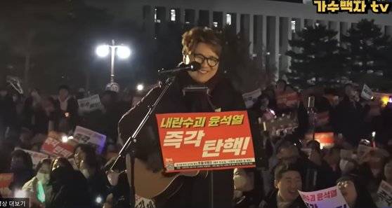 가수 백자가 지난 6일 ‘윤석열 대통령 탄핵 촉구 촛불집회’에서 크리스마스 캐럴 ‘펠리스 나비다’(Feliz Navidad)를 개사한 ‘탄핵이 답이다’를 부르고 있다. 사진 유튜브 가수백자TV 캡처