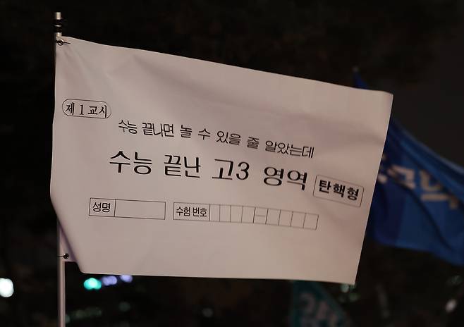 12일 오후 서울 영등포구 국회 앞에서 열린 윤석열 대통령 탄핵 촉구 촛불 집회에 참석한 한 시민이 ‘수능 끝나면 놀 수 있을 줄 알았는데’라고 적힌 깃발을 들고 있다. [연합]