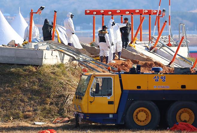 3일 오전 전남 무안군 무안국제공항 제주항공 여객기 참사 현장에서 항공철도사고조사위원회 및 국과수 관계자 등이 방위각시설(로컬라이저)에 파묻힌 엔진에 덮어둔 덮개를 치우고 있다. [연합]