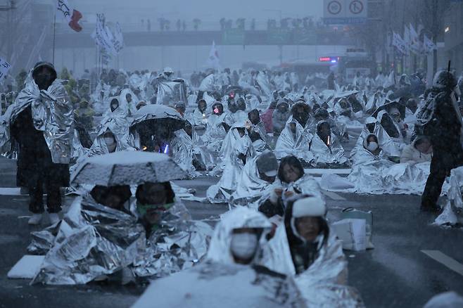 5일 오전 서울 용산구 대통령 관저 앞 도로에 앉은 철야 집회 참가자들이 은박 보온 담요로 몸을 감싸고 눈을 피하고 있다. 이날 오전 7시 30분 서울 전역에는 대설주의보가 내려졌다. /뉴시스