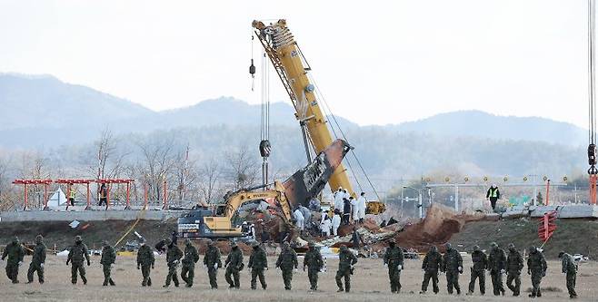 4일 오후 전남 무안국제공항 참사 현장에서 특전사 대원들의 수색 작업 뒤로 방위각시설(로컬라이저)에서 엔진 인양 작업이 진행되는 모습. 사진=뉴스1