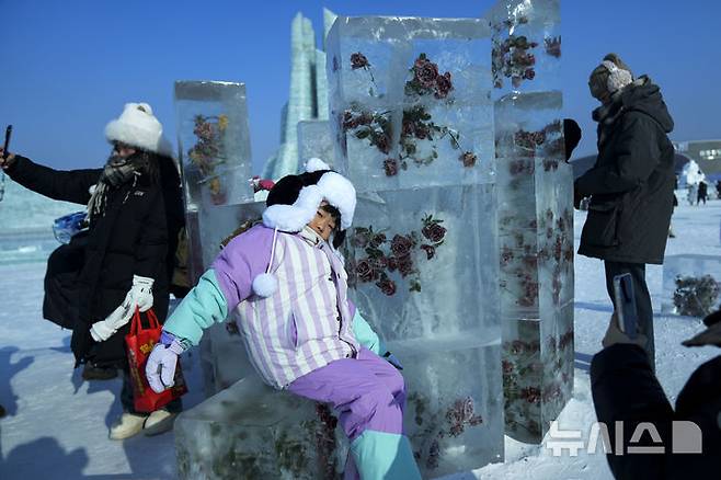[하얼빈=AP/뉴시스] 6일 중국 헤이룽장성 하얼빈에서 열린 제41회 하얼빈 빙설제에서 관광객들이 얼음 조각 옆에서 기념촬영 하고 있다. 2025.01.10.