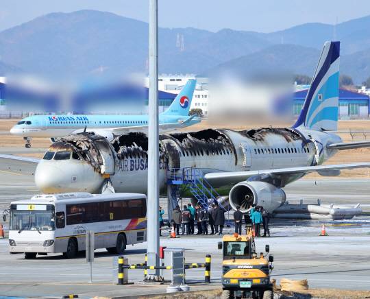 29일 부산 강서구 김해국제공항에서 부산시와 소방당국, 공항 유관기관 관계자들이 에어부산 여객기 화재 현장을 보고 있는 가운데 뒤로 대한항공 여객기가 지나가고 있다. 연합뉴스