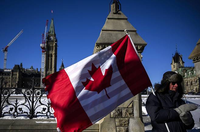 트럼프의 관세 정책에 항의하는 캐나다 시민이 지난 1일(현지시간) 캐나다 오타와에 있는 국회의사당 언덕 밖에서 앞뒤로 겹쳐붙인 캐나다와 미국 국기를 들고 있다. [AP]