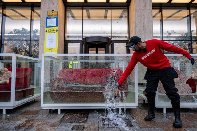 영국 런던의 석유 대기업 쉘 본사 앞에서 12일 국제환경단체 그린피스 소속 환경운동가가 소품이 물에 잠긴 유리 진열장을 깨며 석유 및 가스 산업이 전 세계 사람들의 삶과 생태계를 파괴하는 극심한 기상 현상을 심화시키고 있다는 퍼포먼스를 보이고 있다. 런던=로이터 연합뉴스