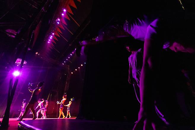 무대에서 화려한 공연이 펼쳐지는 동안 한쪽에서는 다음 무대를 위해 곡예사들이 점프하며 몸을 풀고 있다.