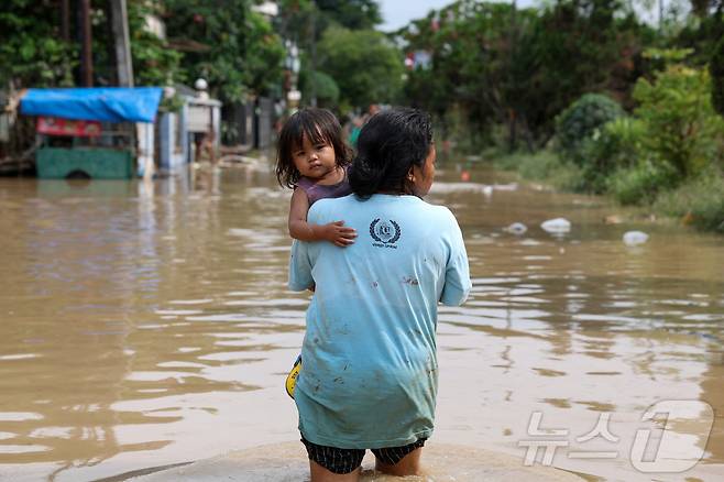 4일(현지시간) 인도네시아 자카르타 외곽 베카시에서 폭우가 내린 후 주택가에 홍수가 발생하자 한 소녀가 어머니에게 실려가고 있다. 2025.3.6 ⓒ 로이터=뉴스1